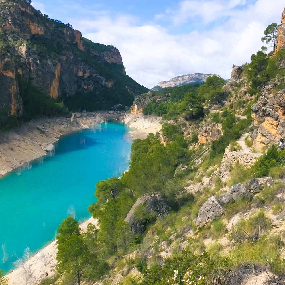 Vista del Embalse de la Fuensanta en Yeste, un lago de aguas turquesas rodeado de montañas y vegetación, ideal para actividades al aire libre y relajación en plena naturaleza.